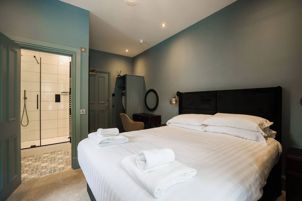 Una habitación de hotel con una cama, un baño con ducha y un escritorio con silla.