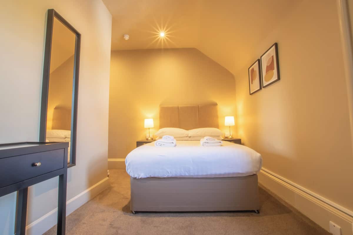 Una habitación de hotel con cama, lámparas de noche, espejo y mesita de noche.
