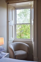 A corner room with a window, a chair, and a bedside table.