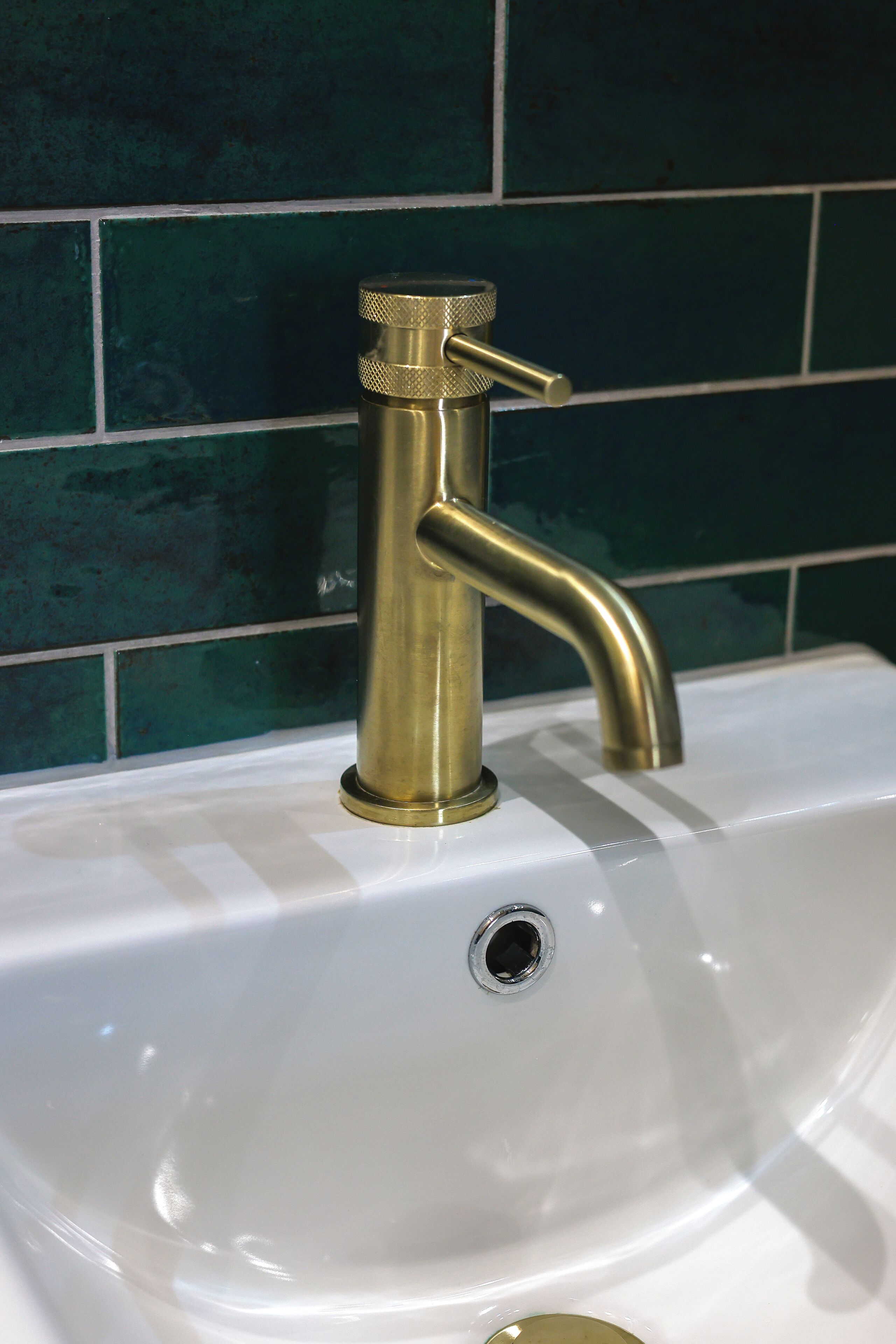 A white sink with a brass faucet and a green tiled backsplash.