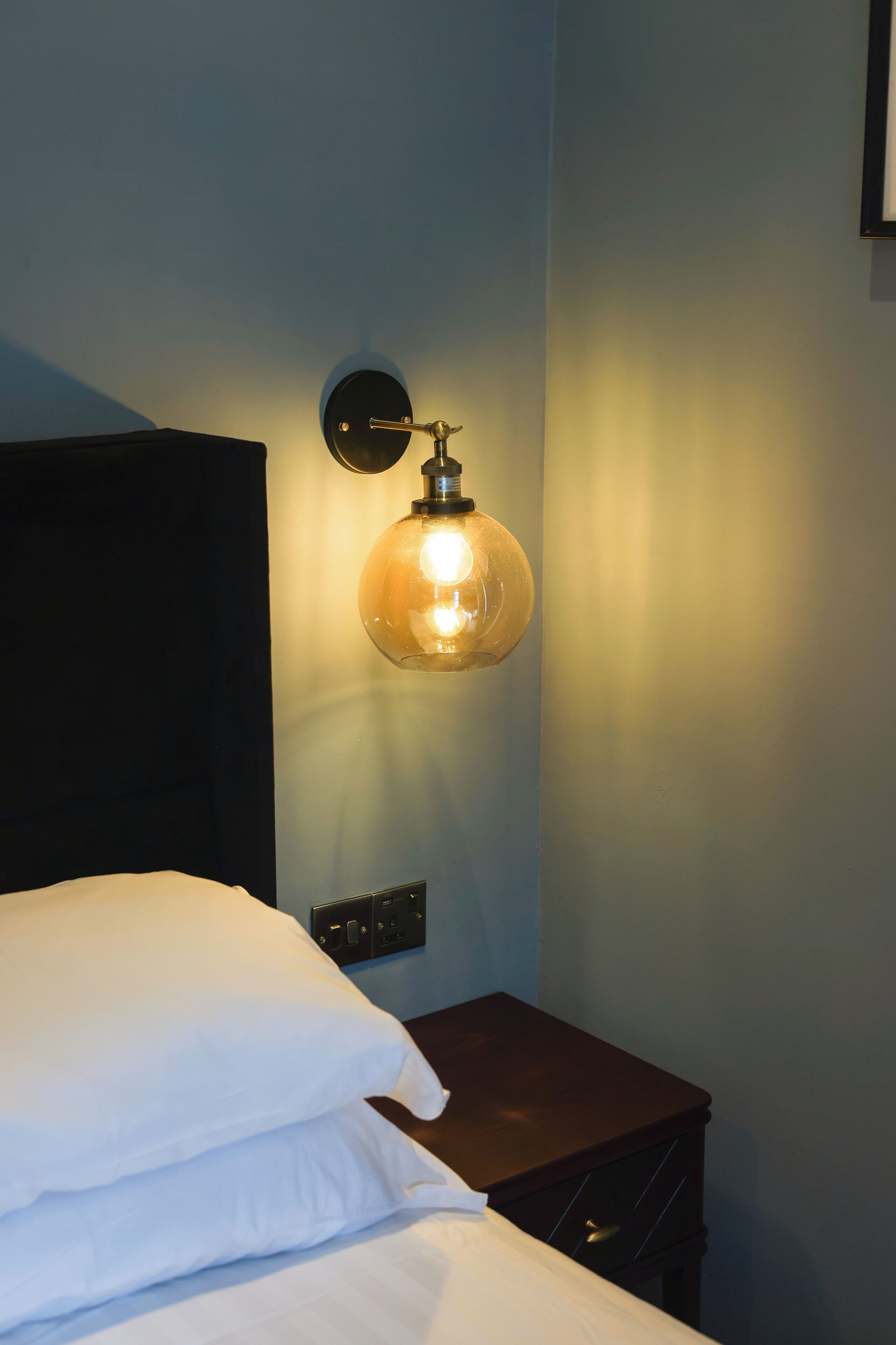 A neatly made bed with white linens and a small bedside table with a lamp.