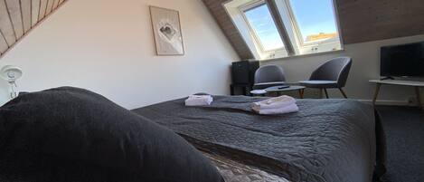Une chambre à coucher comprenant un lit, un bureau, deux chaises, un téléviseur et une fenêtre de toit.