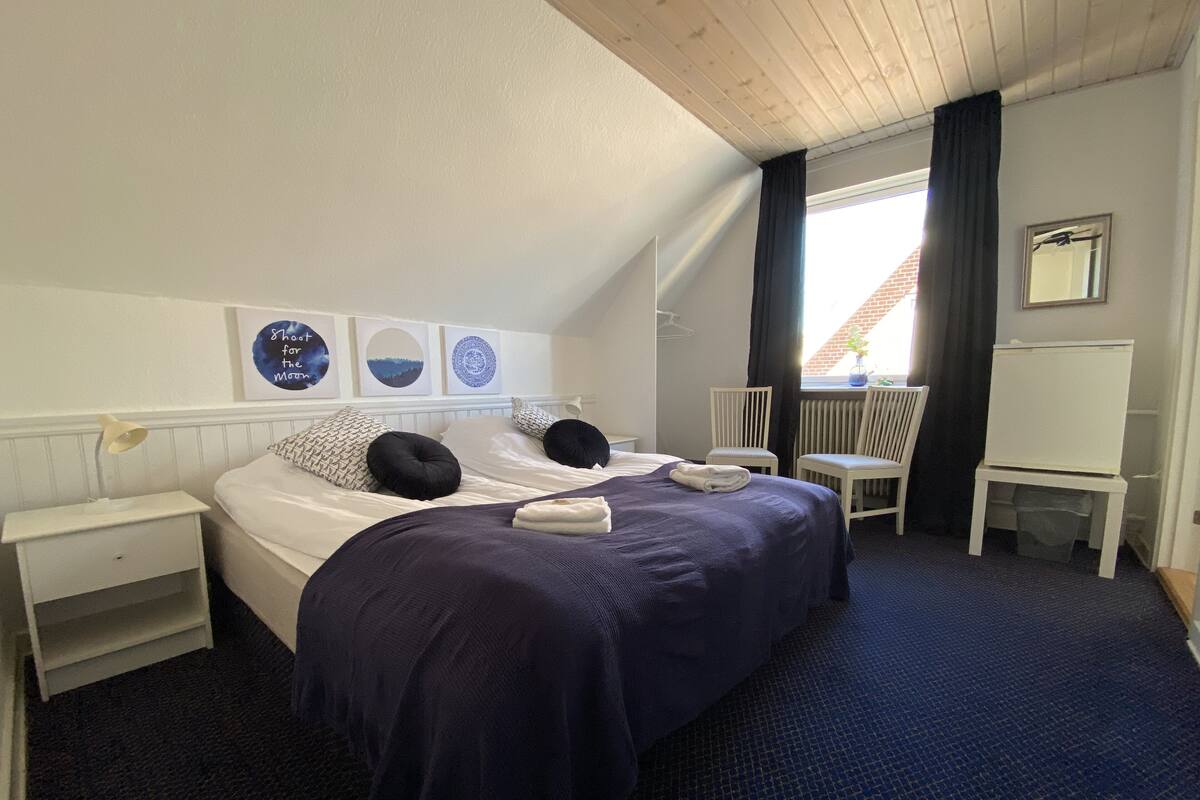 Ein ordentlich eingerichtetes Hotelzimmer mit Bett, Nachttischen, einem Sessel und einem kleinen Schreibtisch.