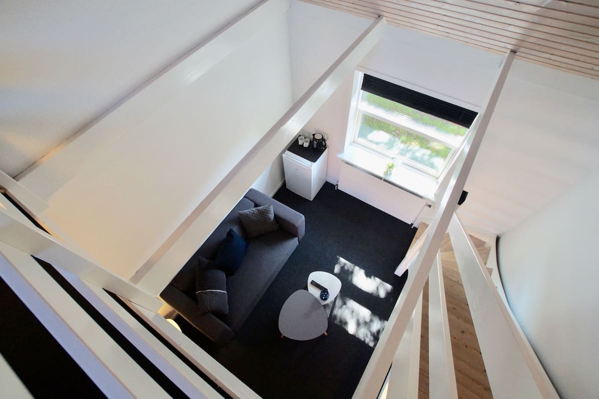 Ein kleines Zimmer mit einer Couch, einem Tisch und einem Fenster mit Blick auf Grünflächen.