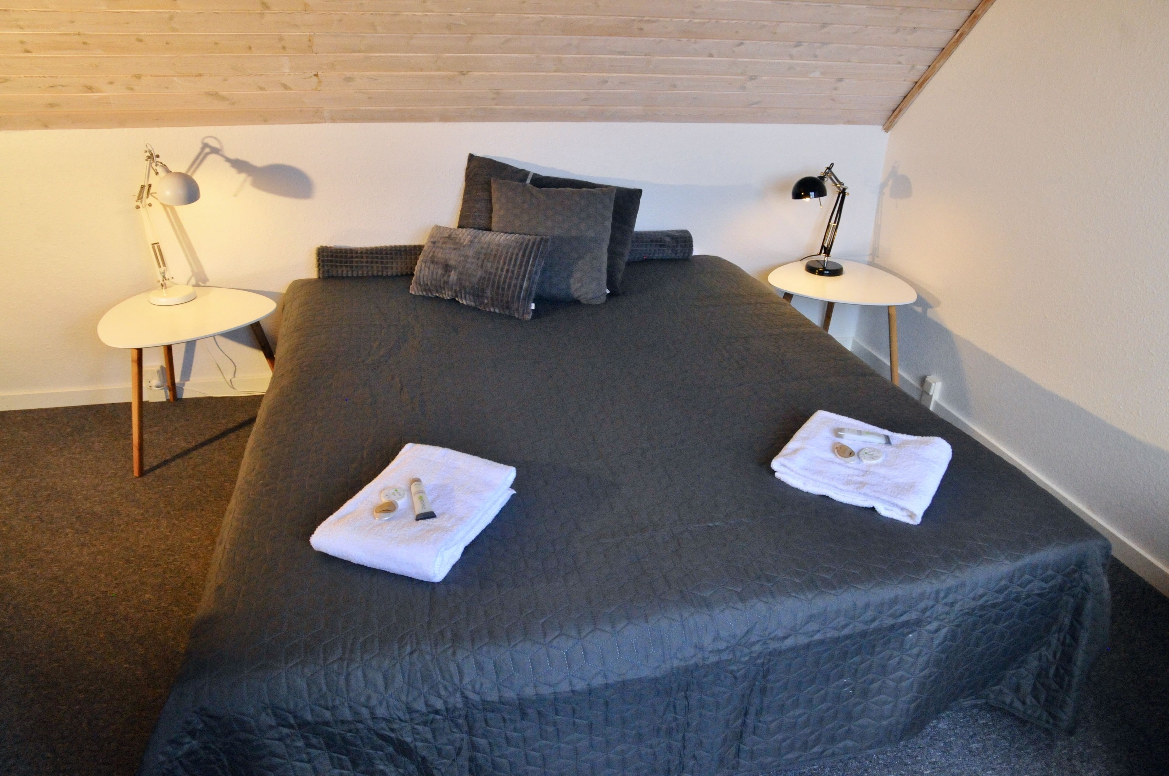 A neatly made bed with a dark quilt, two bedside lamps, and a pillow on a headboard.
