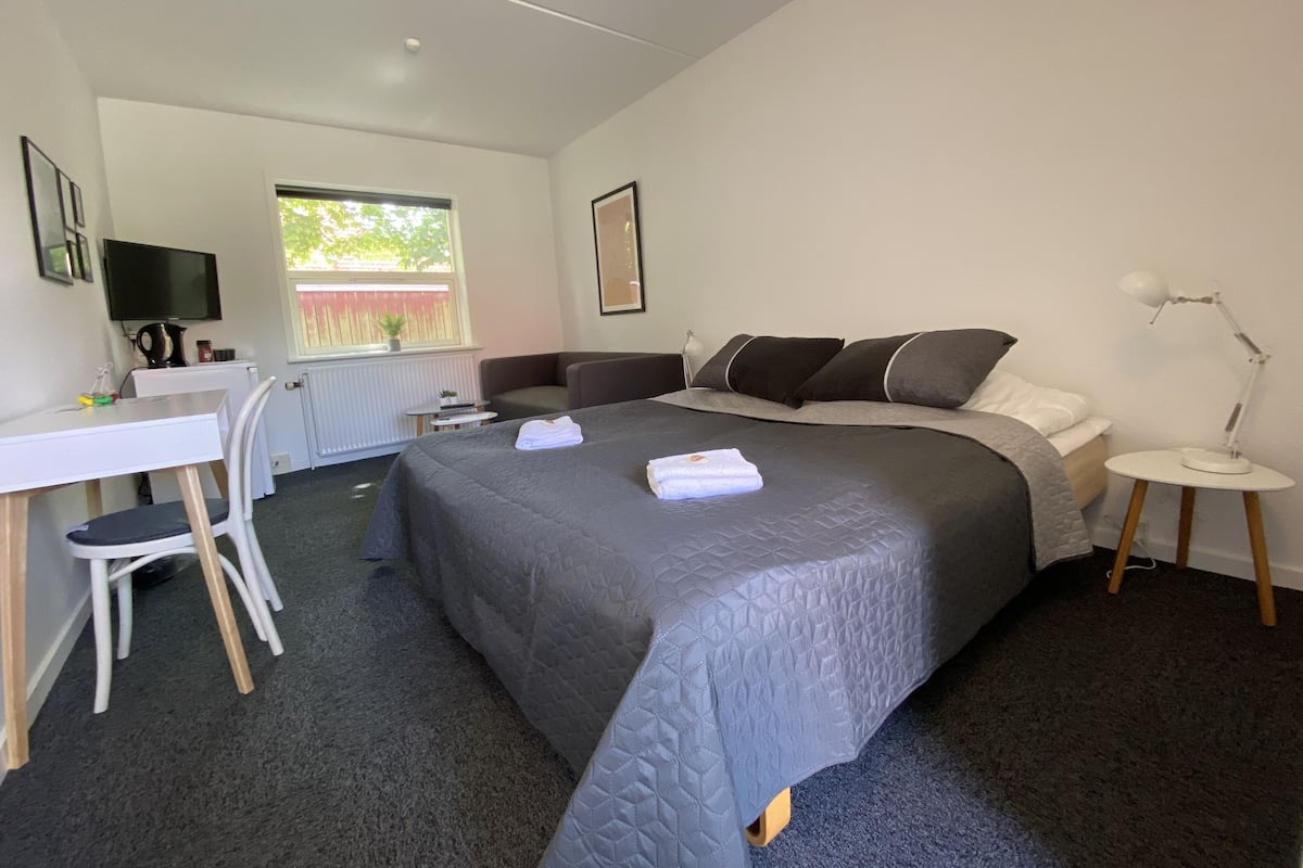 Ein Schlafzimmer mit Bett, Schreibtisch, Stuhl, Fenster und Nachttisch mit Lampe.