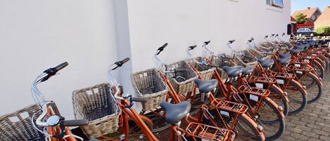 A row of orange bicycles with wicker baskets, parked against a white building with windows.