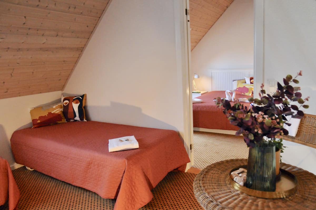 Ein Schlafzimmer mit einem Bett, einem Spiegel, einem Nachttisch und einer Vase mit Blumen.