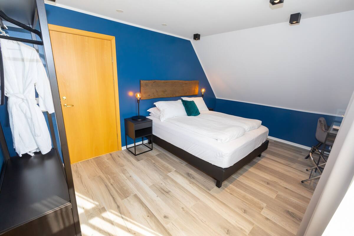 Un dormitorio con cama, cabecero de madera, mesita de noche, una silla y un armario.
