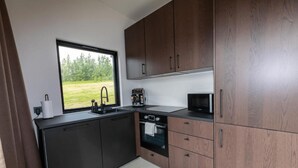 A compact kitchen with a window, a coffee maker, a microwave, and wooden cabinets. - Hotel North (Akureyri)