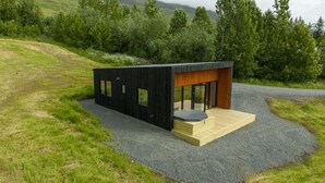 A modern, black wooden cabin with a wooden deck and a small patio area. - Hotel North (Akureyri)