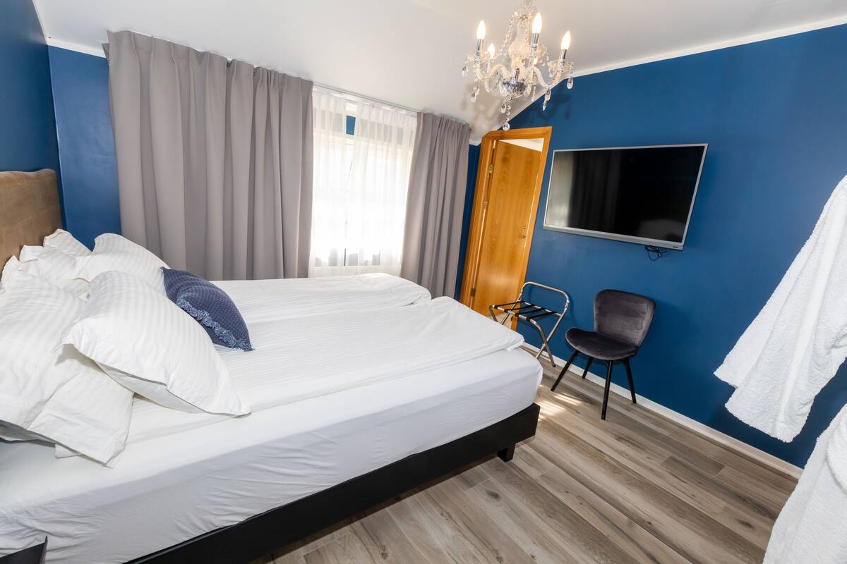 Una habitación de hotel con una cama grande, un televisor montado en la pared, piso de madera y un candelabro.