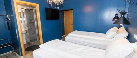 A hotel room with a shower, a bed with white bedding, a chandelier, and a flat-screen TV.
