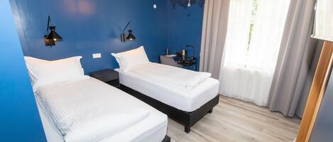 A hotel room with two beds, a chandelier, a nightstand, and a window with curtains.