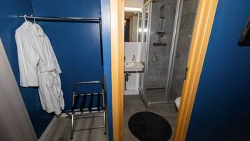 A bathroom with a shower, a towel rack with robes, and a small chair.