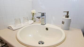 A bathroom with a white sink, a modern faucet, a glass soap dispenser, and a vase with a white flower.
