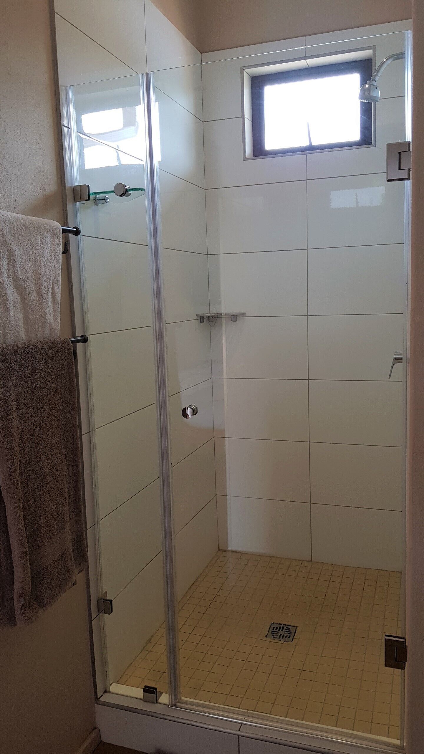 A glass-enclosed shower with a small window, tiled walls, and a visible drain.