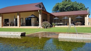 A building with a covered patio area, outdoor seating, and a small pond with water features. - Esther's Country Lodge (Magaliesberg)