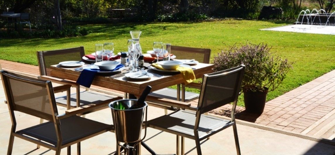 An outdoor dining area with a table set for four, surrounded by chairs, a metal pot, and a potted plant.