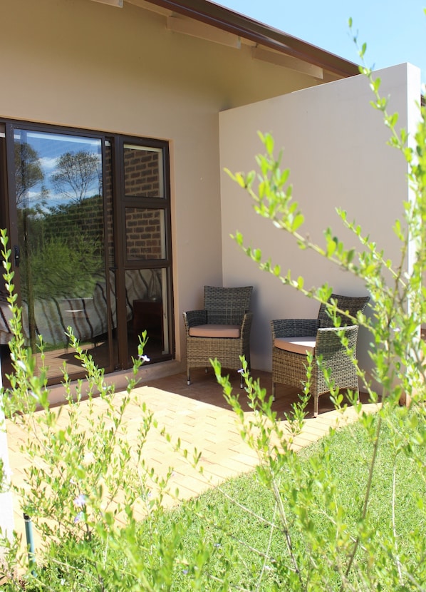 A patio area with wicker furniture, a glass door leading outside, and a view of the surrounding greenery. - Esther's Country Lodge (Magaliesberg)
