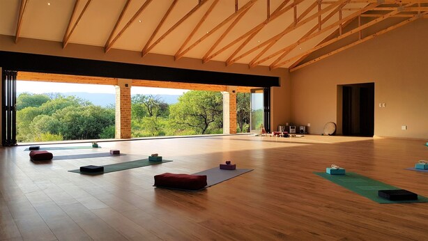 A spacious room with wooden floors, yoga mats, and blocks, large windows with a view of trees and mountains. - Esther's Country Lodge (Magaliesberg)
