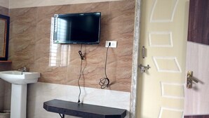A bathroom with a sink, mirror, television mounted on the wall, and a door with geometric patterns. - Sree Guru Sannidhi A Budget Luxury Lodge (Mantralayam)