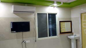A bathroom with a wall-mounted air conditioner, a window with a metal grill, a sink, and a mirror. - Sree Guru Sannidhi A Budget Luxury Lodge (Mantralayam)