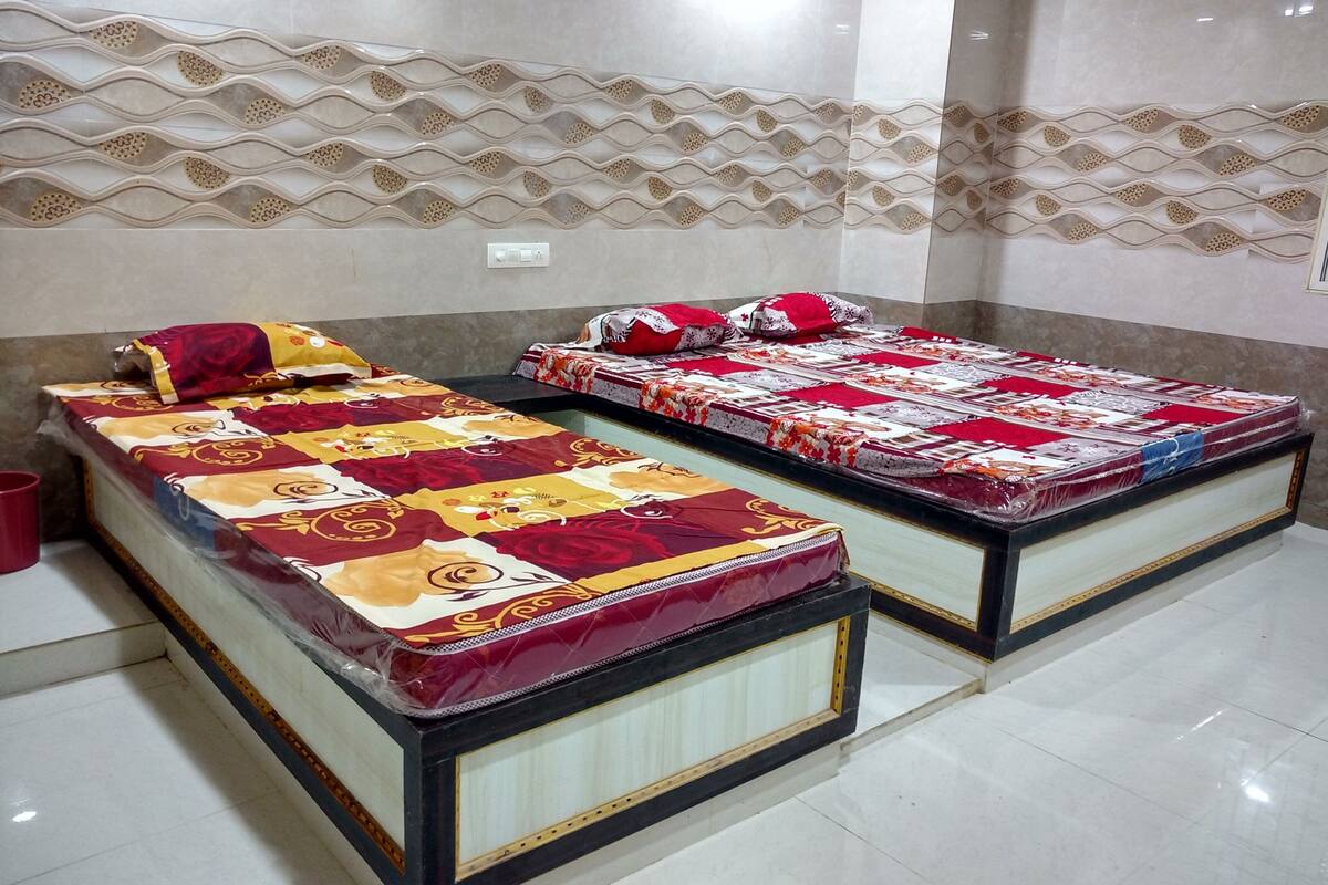 Two beds with patterned bedding, a tiled floor, and a decorative wall.
