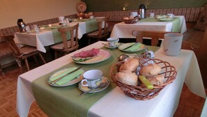 Un espace repas avec des tables mises pour le petit-déjeuner, comprenant des assiettes, du pain et des tasses à thé.