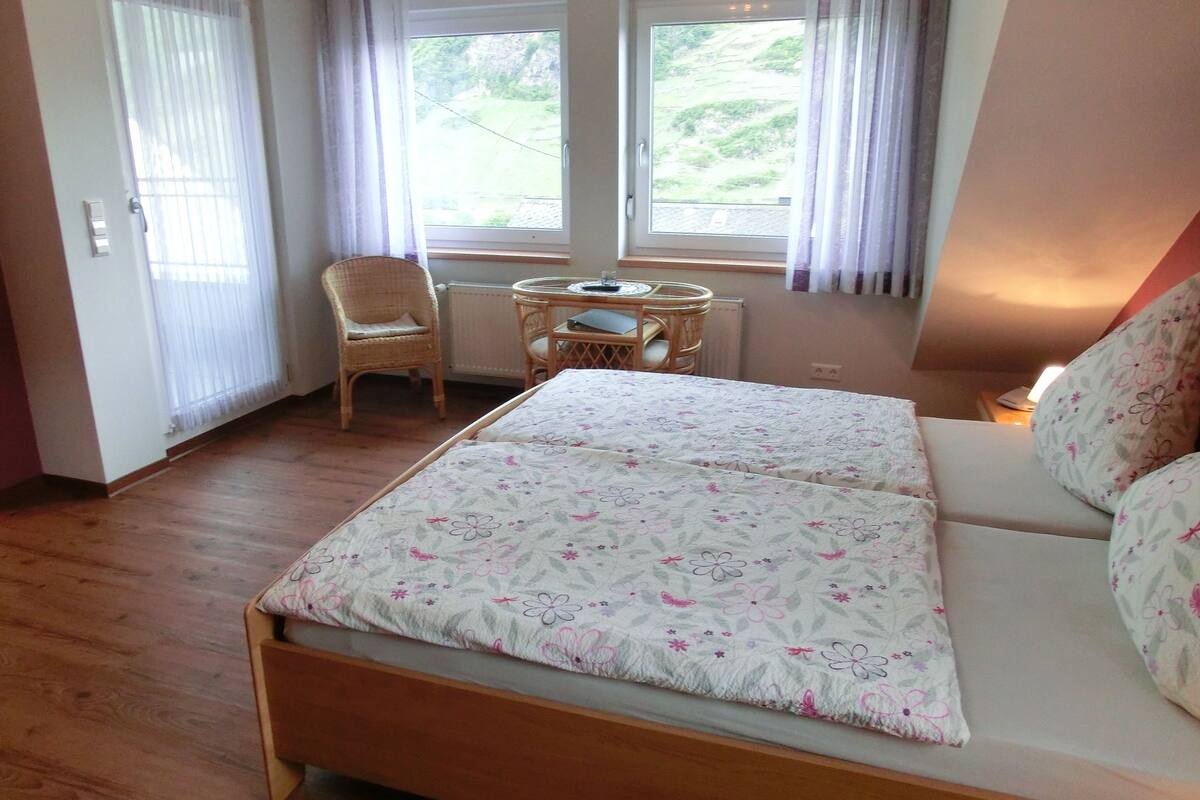 Un dormitorio con cama, una silla, una mesa y vistas al exterior a través de las ventanas.