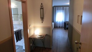 Un couloir étroit avec un plancher en bois, une petite table avec une lampe, un miroir au mur et une porte donnant sur une salle de bain.