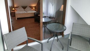 Une chambre à coucher comprenant un lit, une chaise, une petite table et donnant sur une autre pièce.