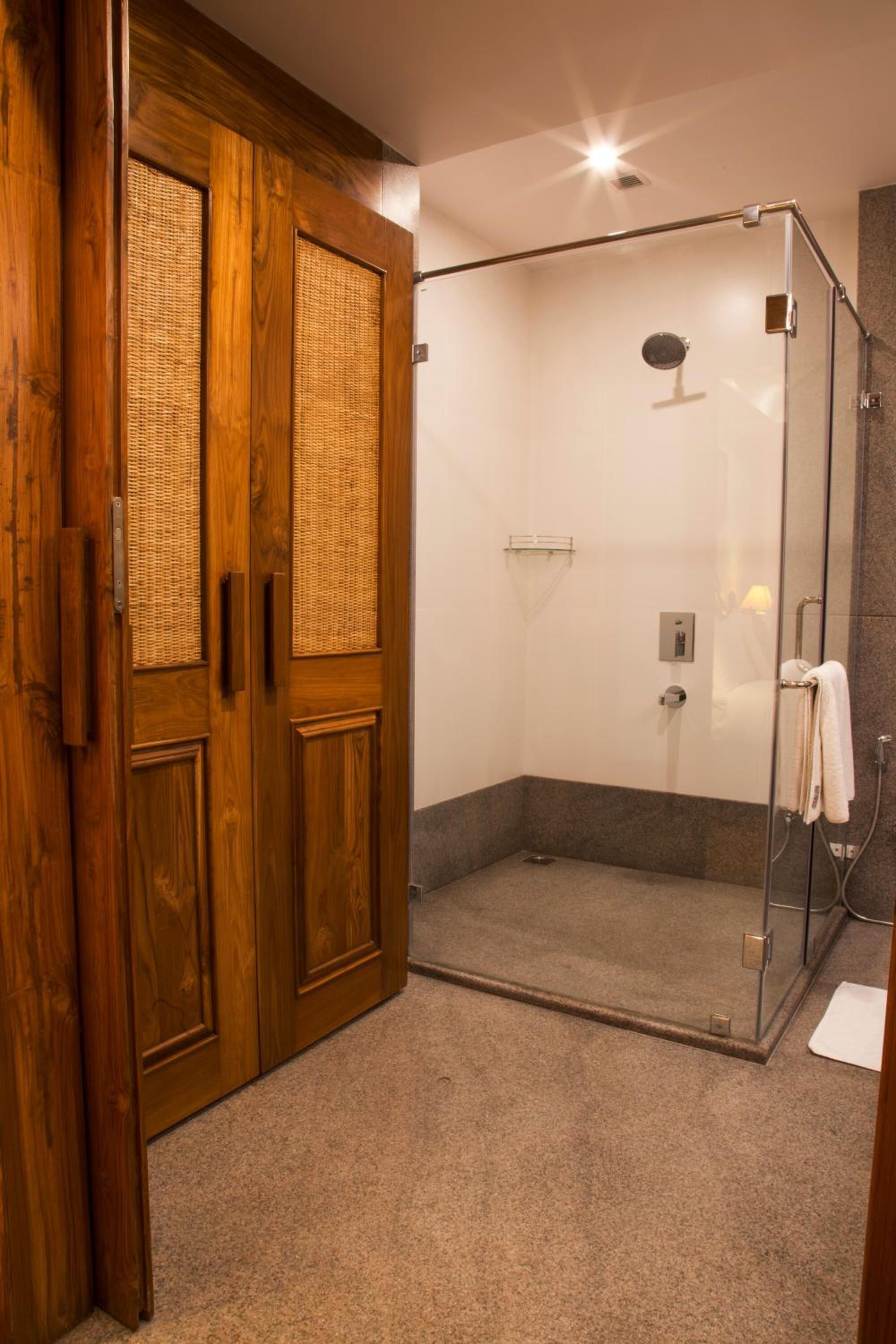 Un baño moderno con ducha de vidrio, puerta de madera con paneles tejidos y un perchero para toallas.