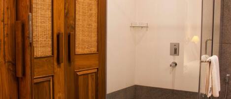 Un baño moderno con ducha de vidrio, puerta de madera con paneles tejidos y un perchero para toallas.