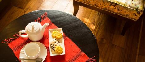 A round table with a white teapot, a white cup, and a plate with a spoon on a red placemat. There is a small rectangular dish with yellow and black items on the table.