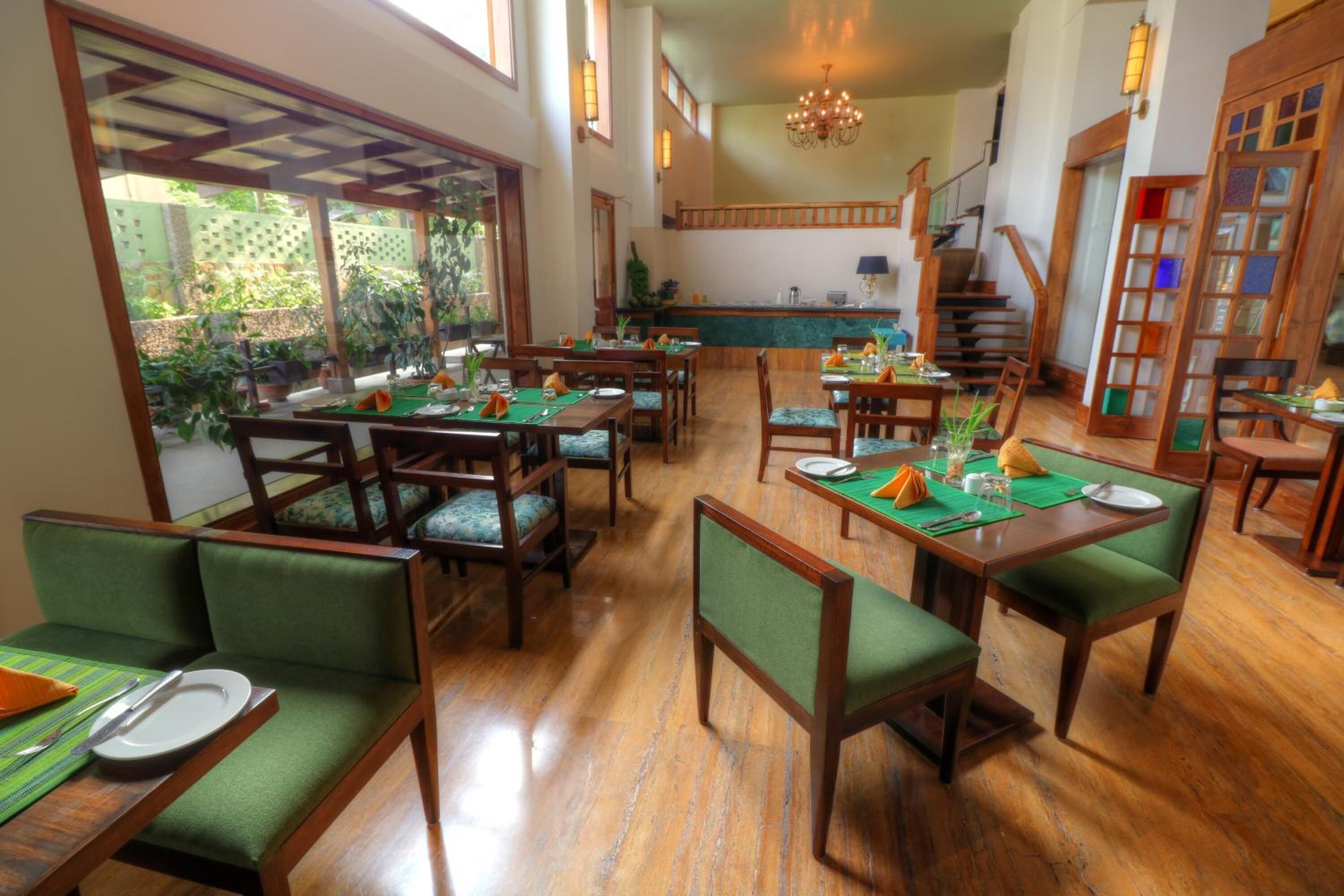 Un ristorante con arredi in legno, sedie imbottite verdi, una zona bar e una scala.