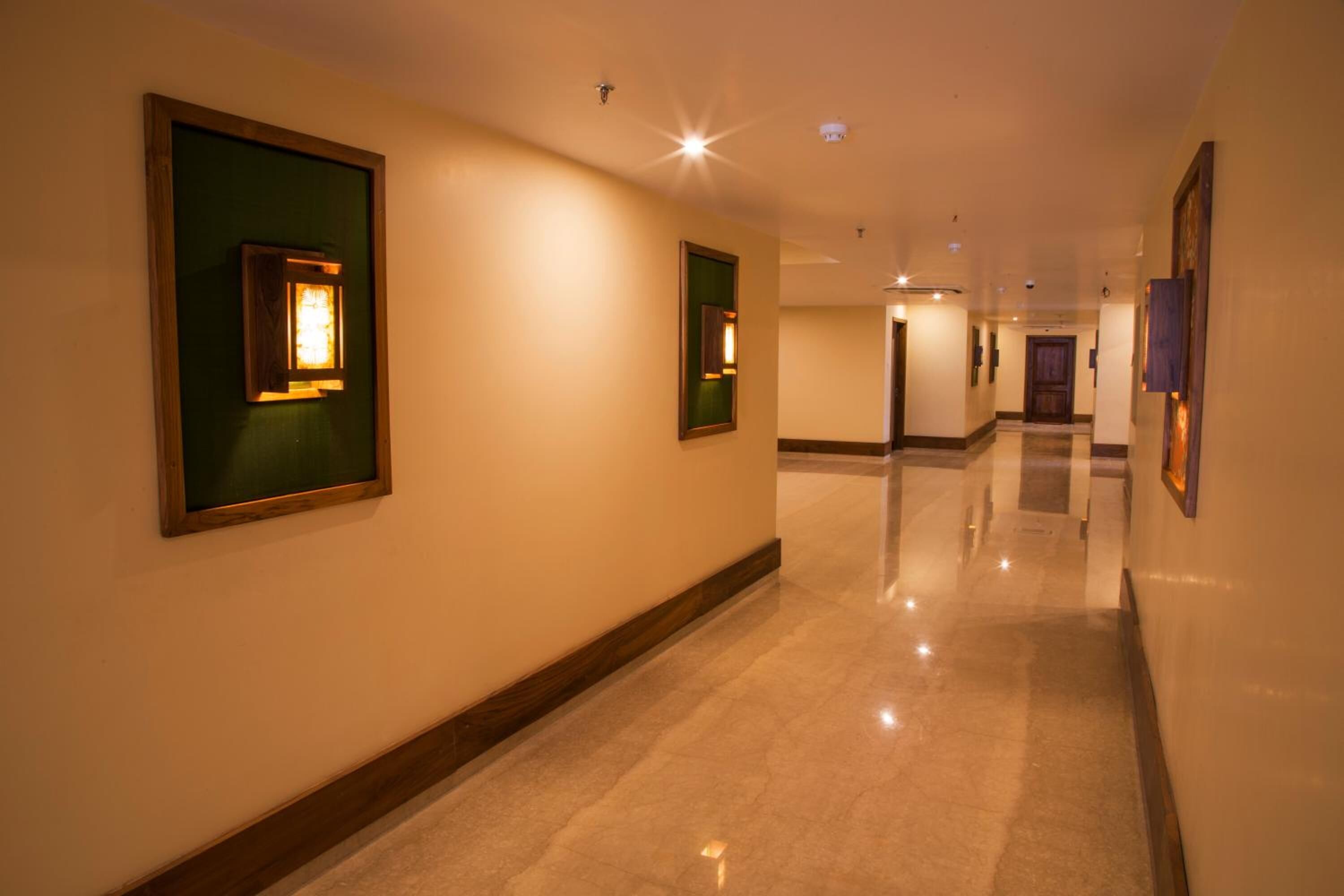 A hotel corridor with framed artwork on the walls, a polished marble floor, and a well-lit ceiling.