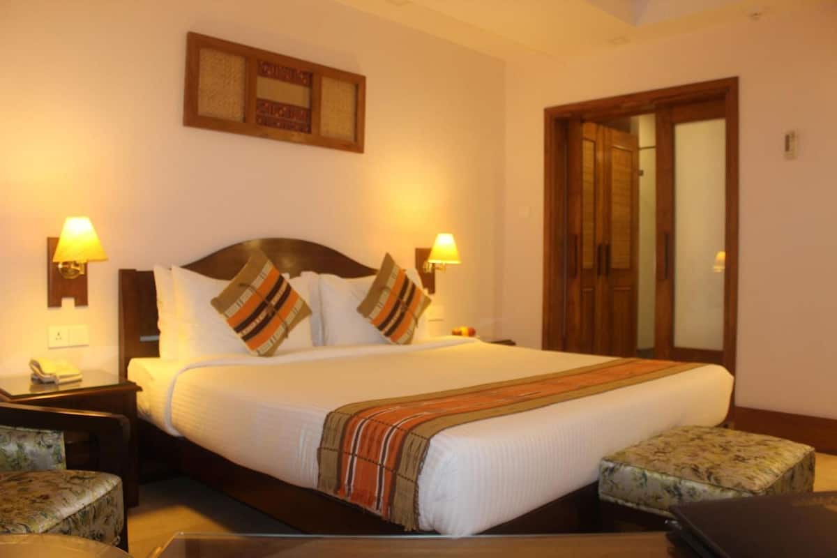 A hotel room with a bed, two bedside lamps, a nightstand, a telephone, a mirror, and a door.