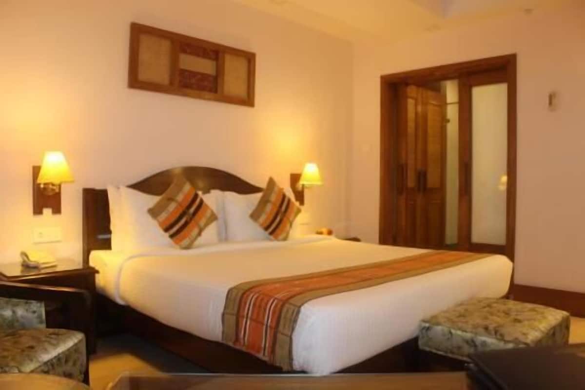 A hotel room with a bed, two bedside lamps, a nightstand, a chair, and a wooden door.