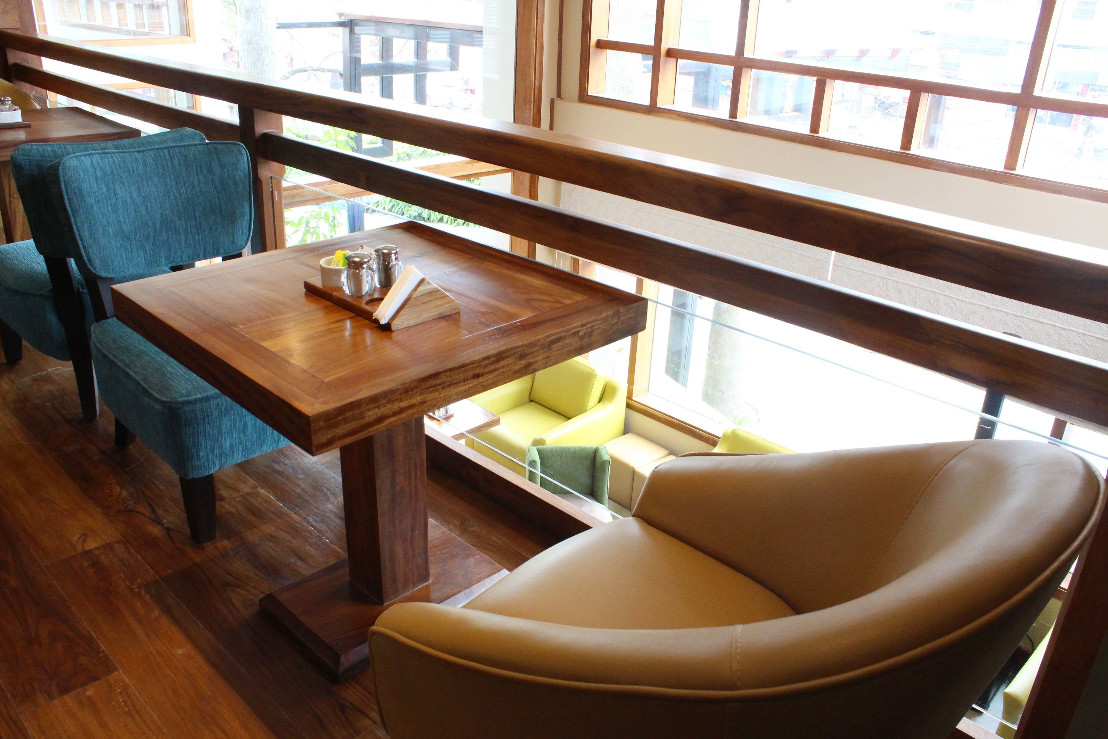 A restaurant interior with a wooden table, a blue chair, a beige chair, and a view through a window.
