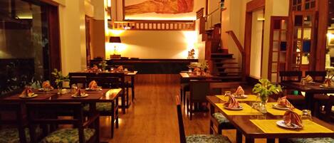 A spacious dining area with wooden tables and benches, a staircase in the background, and a large wall mural.