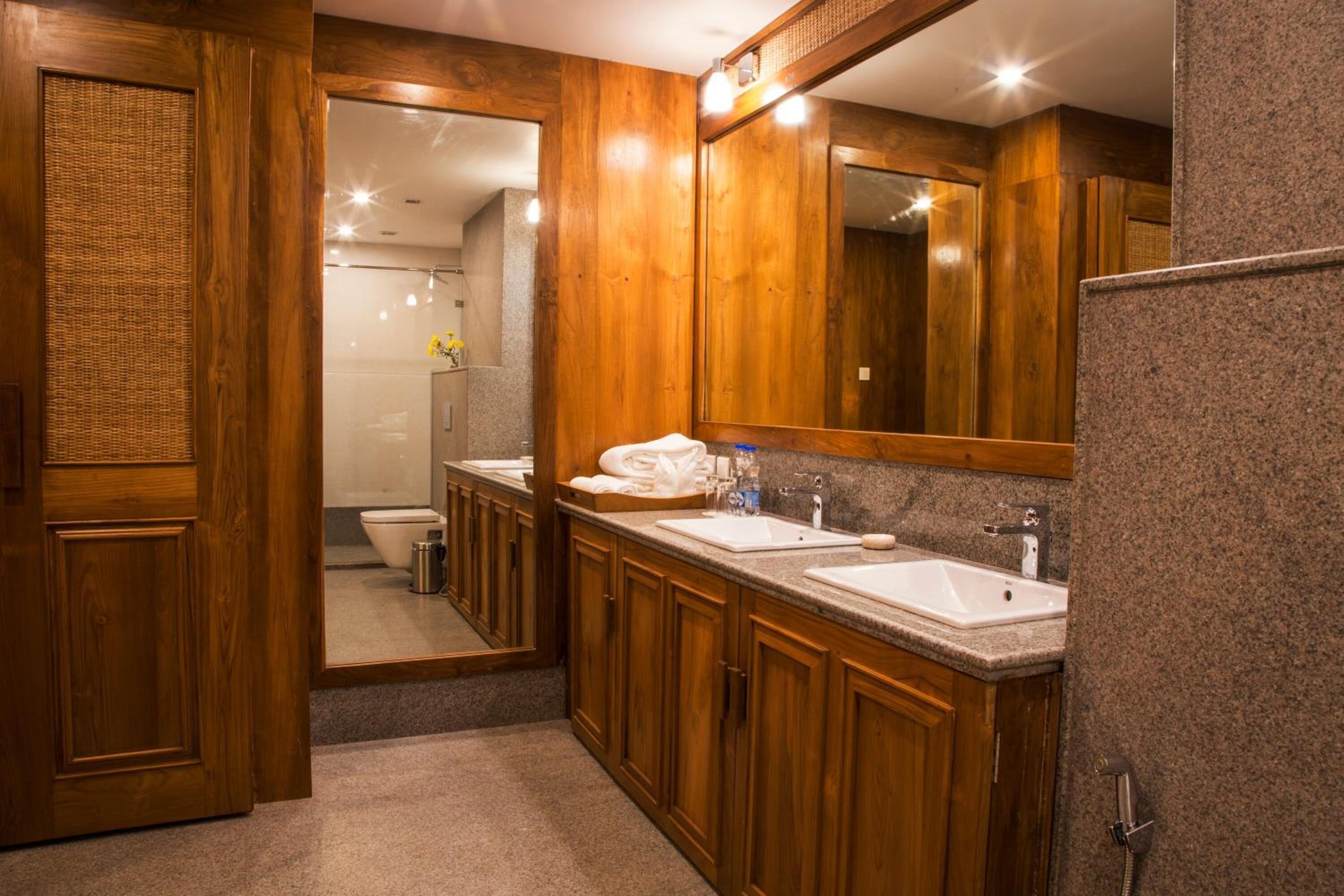 A wooden bathroom with two sinks, a large mirror, and a shower area.