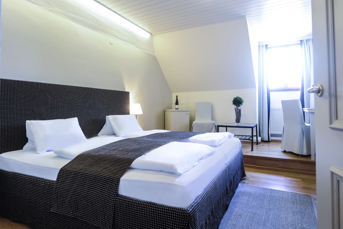 Une chambre d’hôtel moderne avec un grand lit, un bureau, une chaise, une petite table et une plante en pot.
