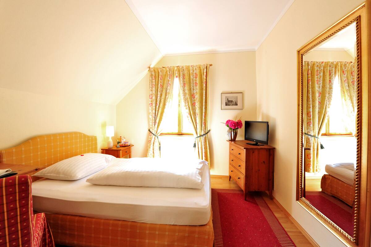 Une chambre d’hôtel avec un lit, une commode, une télévision, une lampe et un grand miroir.