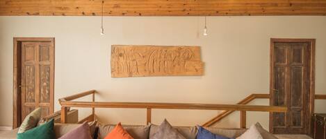 Een houten plafond met inbouwspots, een houten trap en een aan de muur hangend kunstwerk.