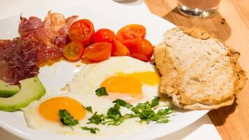 A breakfast plate with eggs, bacon, tomatoes, avocado, and toast on a wooden table.