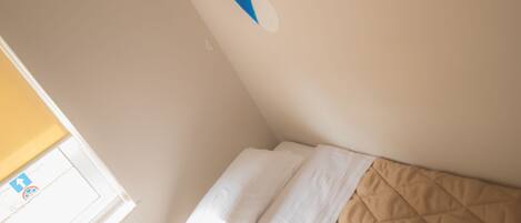 A bedroom with a bed, a wall-mounted shelf, and a window with blinds.