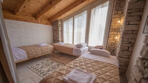 A room with two beds, a stone wall, wooden beams, and a window with curtains. - Mosaic Home - Hostel (Tirana)