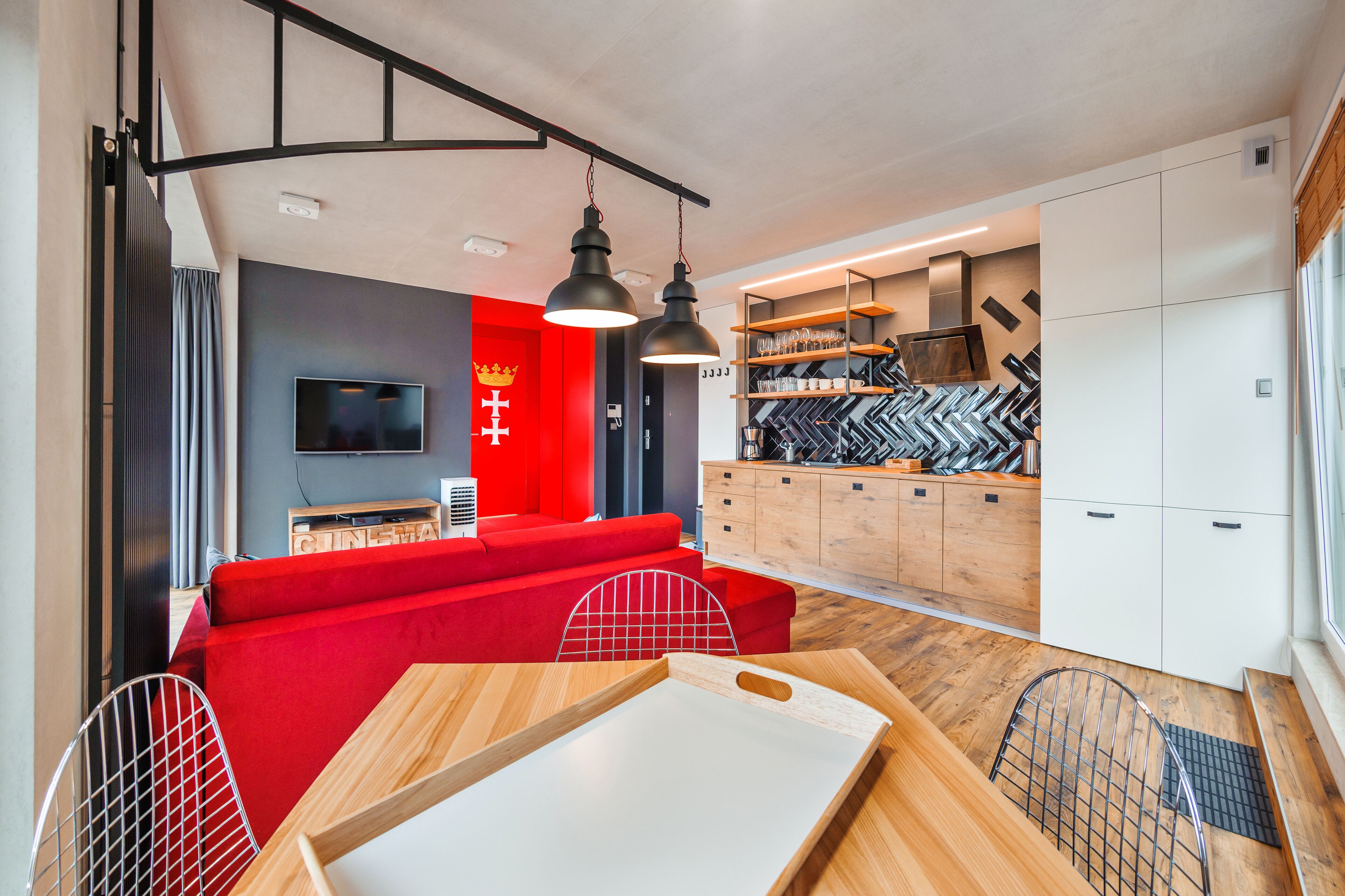 A modern kitchen with a red sofa, wooden cabinets, and a TV.