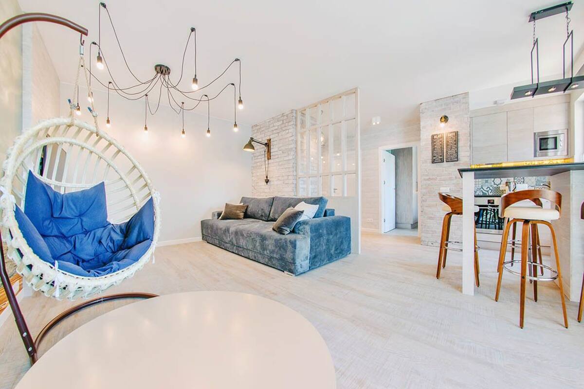 Un salon moderne avec un canapé bleu, un fauteuil suspendu et un coin cuisine doté de tabourets de bar.